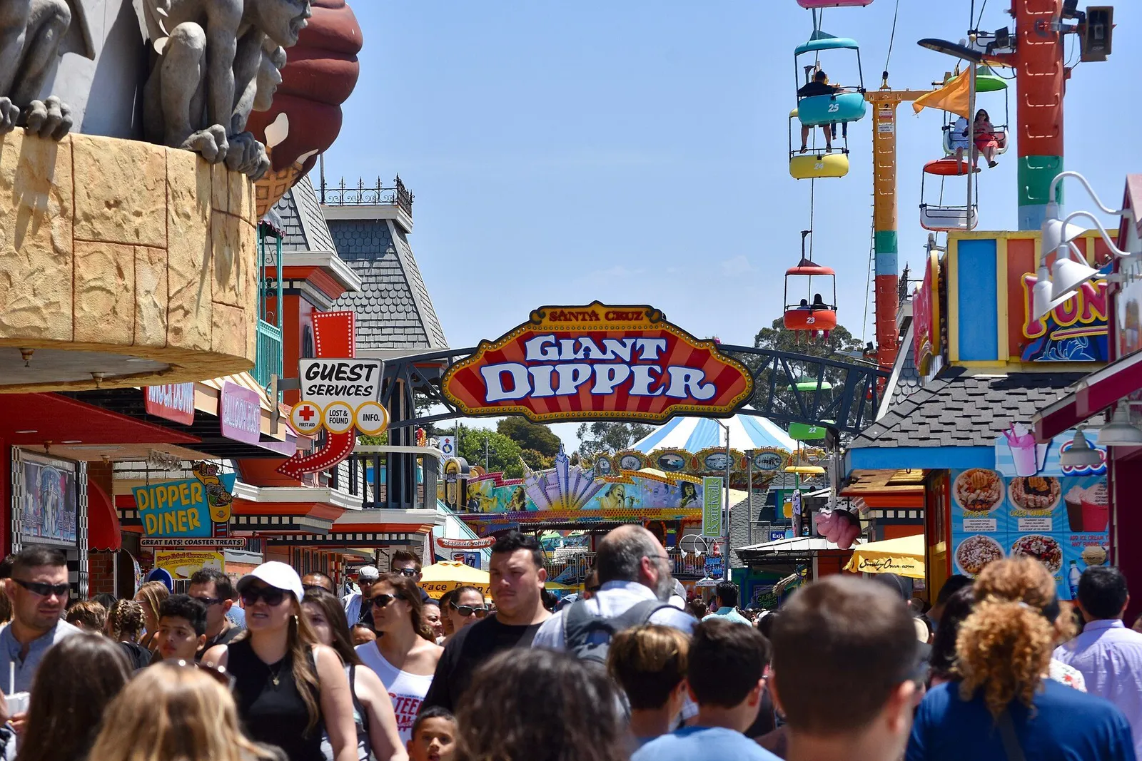 Parents walking with a stroller and two children toward theme park entrance gates on a sunny day