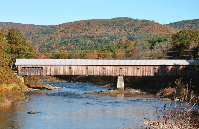 Red and orange maple foliage around a New England church steeple and covered bridge in autumn