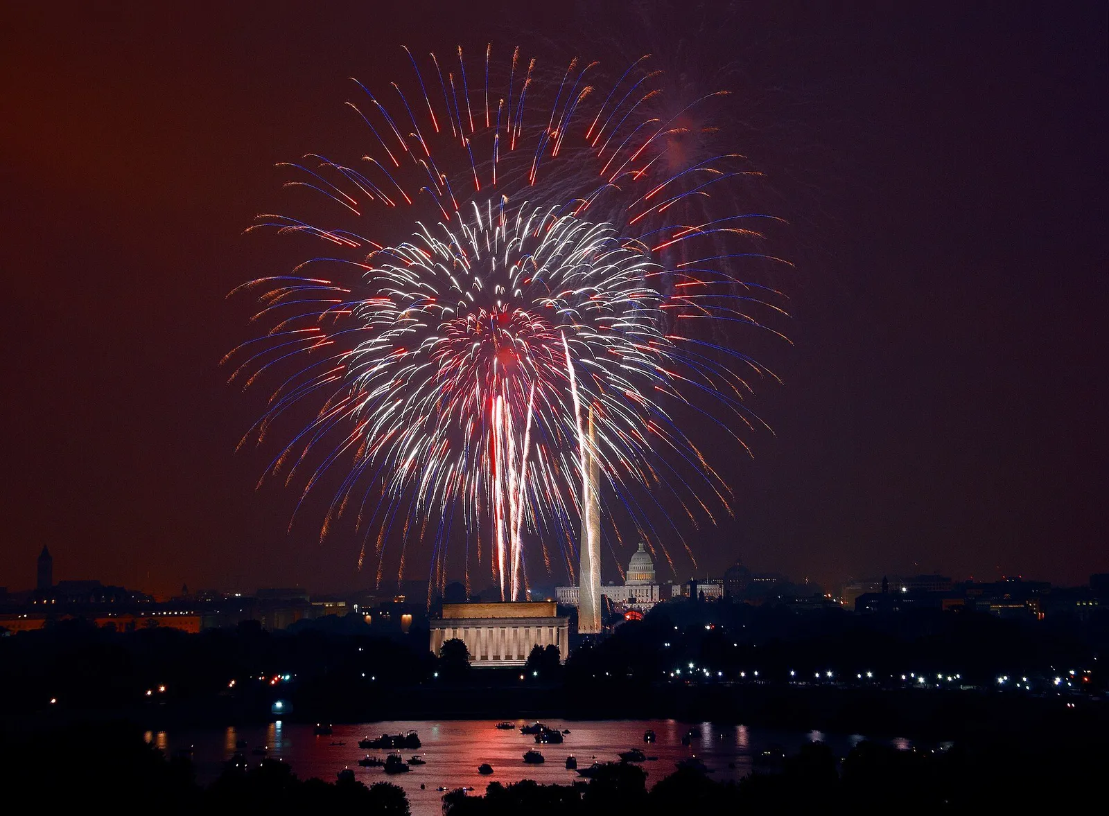Fireworks bursting over a riverfront crowd celebrating the Fourth of July