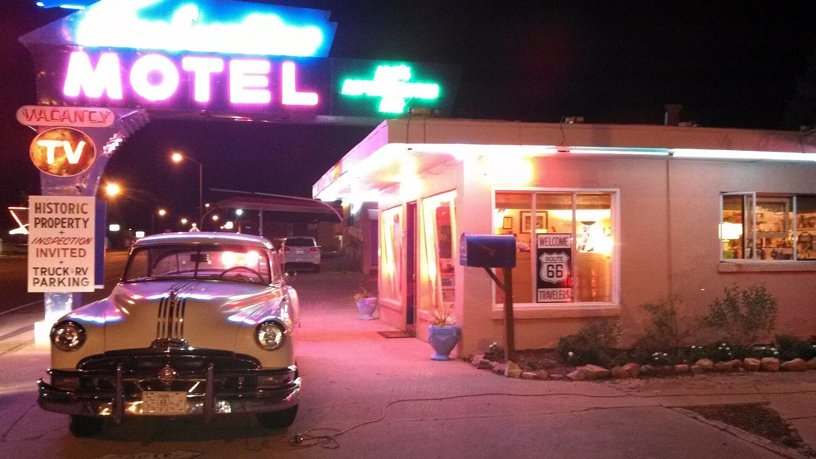 A vintage Route 66 highway shield sign beside a neon roadside sign at dusk