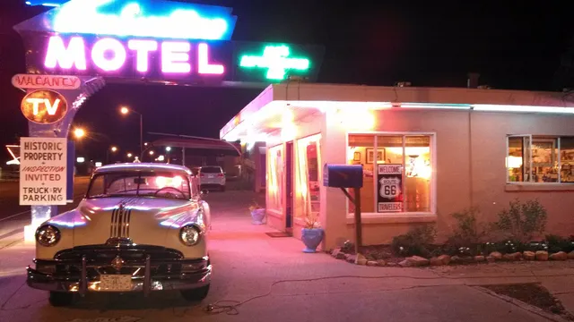 A vintage Route 66 highway shield sign beside a neon roadside sign at dusk